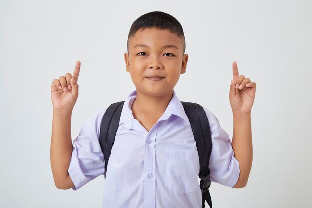 A young Asian cute boy standing in a Thai school uniform with a backpack bag and book on a white background banner