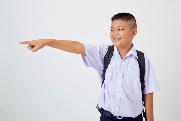 Foto un giovane ragazzo carino asiatico in piedi in un'uniforme scolastica thailandese con una borsa zaino e un libro su uno striscione bianco sullo sfondo