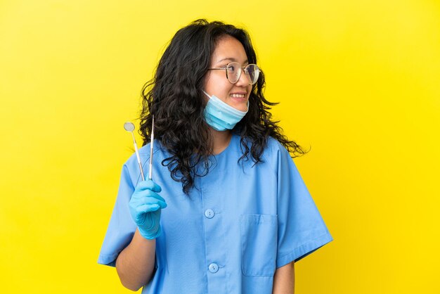 Giovane dentista asiatico che tiene gli strumenti su sfondo isolato guardando side
