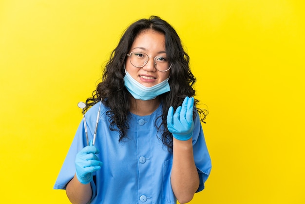 Young asian dentist holding tools over isolated background making money gesture