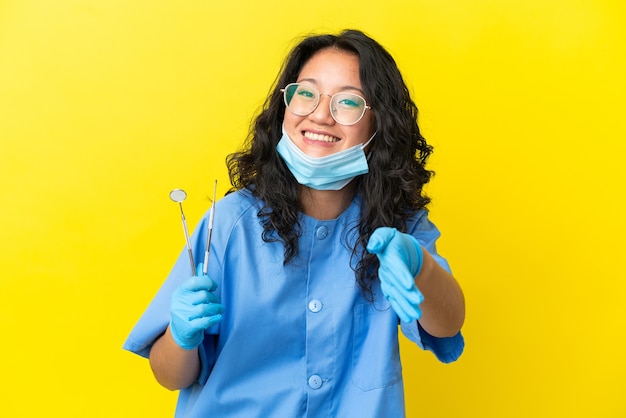 Giovane dentista asiatico che tiene gli strumenti su uno sfondo isolato che stringe la mano per chiudere un buon affare