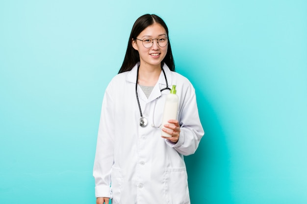 Молодая азиатская девушка дерматолога счастливая, усмехаясь и жизнерадостная.