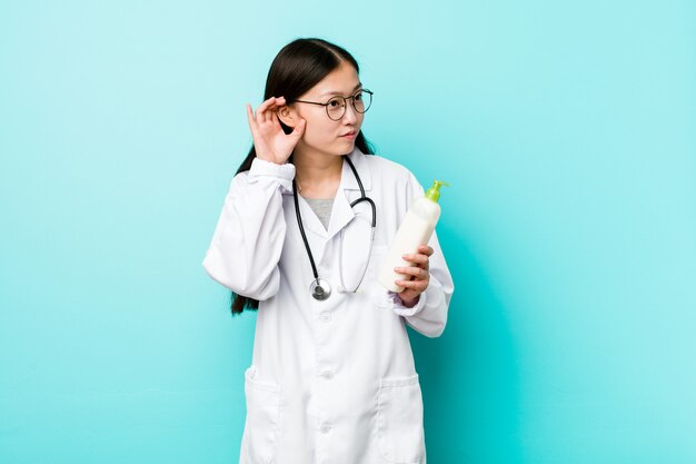 Young asian dermatologist girl trying to listening a gossip.