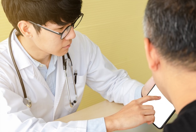 Young asian doctor explaining with male patient over  digital tablet in office