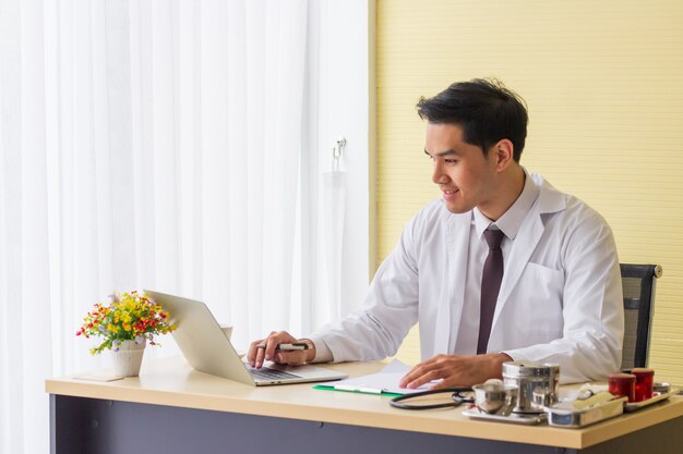 A young Asian doctor is smiling and working on the hospital desk.