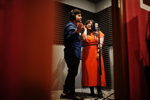 Young asian duet singers with microphone recording song in record music studio.