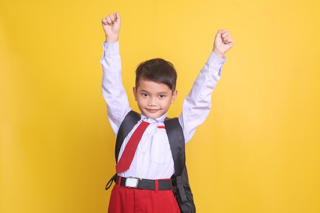 Young asian elementary student in school uniform raising hands up showing winning gesture