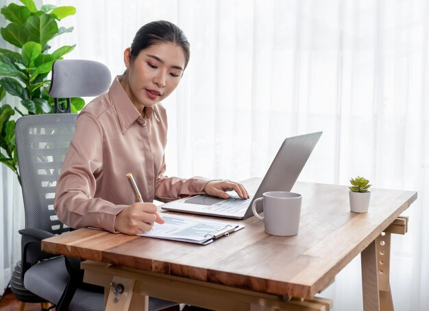 Young asian enthusiastic businesswoman at modern office desk with laptop