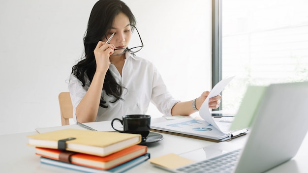 Young asian entrepreneur cogitating thinking making important decision at workplace. Concentrated serious office worker millennial woman analysing results