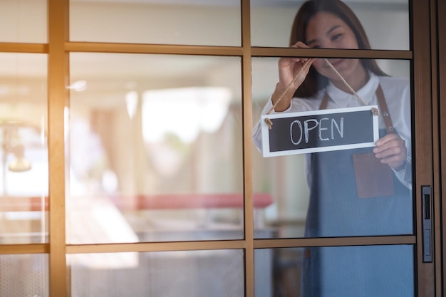 A young asian entrepreneur or a waitress hanging open sign on the shop front door