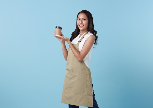 Young asian entrepreneur woman in apron with hand holding cup of coffee isolated on blue background