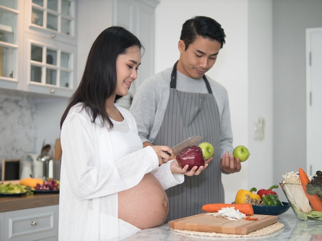 Young asian expecting pregnant couple cooking together in the kitchen at home.