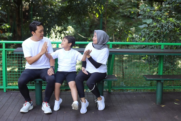 若いアジアの家族の愛、緑豊かな公園で笑顔で話して座っている父母と息子。親lookin