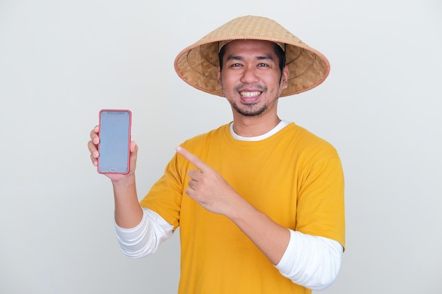 Young asian farmer smiling happy while pointing to blank phone screen that he hold