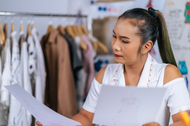 若いアジアのファッションデザイナーやテーラーの女性が手に服のスケッチをチェック