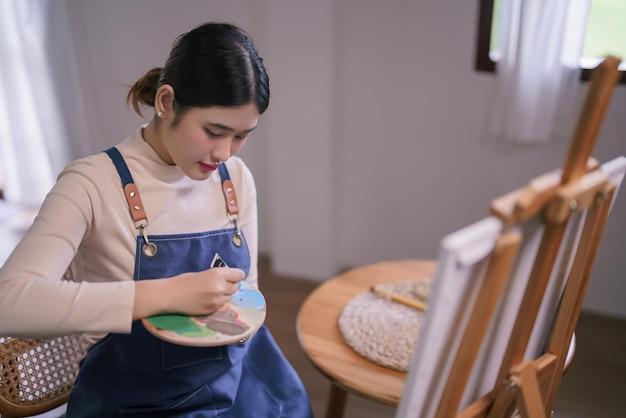 젊은 아시아 여성 예술가 는 캔버스 에 그림 을 그리기 위해 컬러 팔레트 에 튜브 에서 색 을 압축 한다