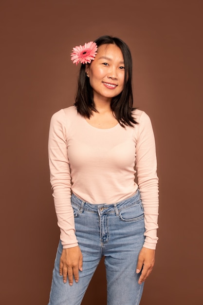 Young Asian female in blue jeans and white pullover keeping arms in front of herself while standing in front of camera against brown background