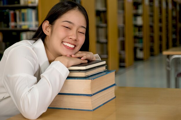 Young Asian female college student research and learn from textbooks shelf in the university library