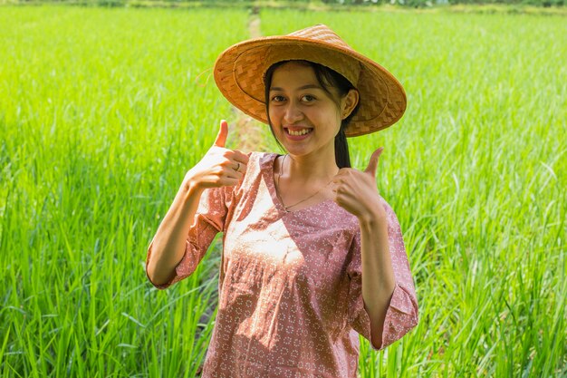 田んぼで親指を示す若いアジアの女性農家