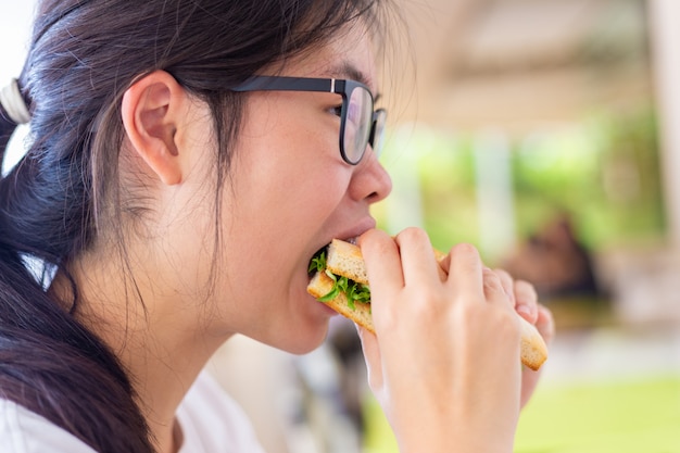 Молодая азиатская женщина держа ее salmon сандвич пока ел вкусно