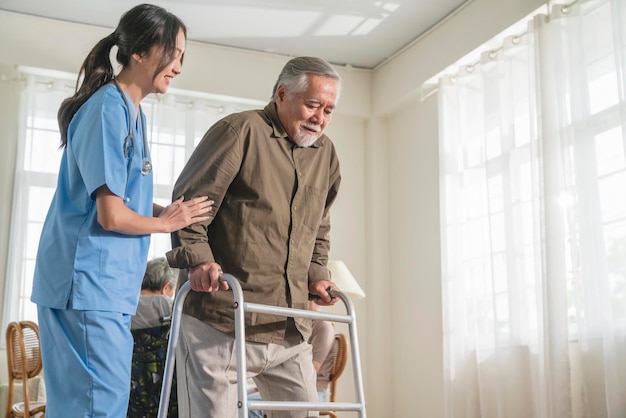 Young asian female nurse care giver helping asian senior old man with mobility walker in living area of nursing home senior daycare centerNurse take care elderly patient with cheerful concentrate