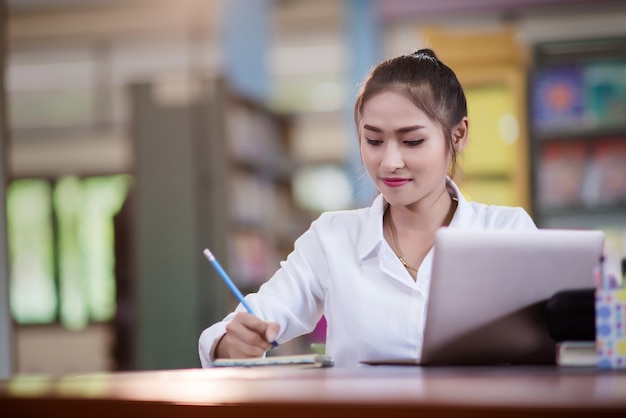 テーブルに座って、ノートブックで書く若いアジア人女性の学生。