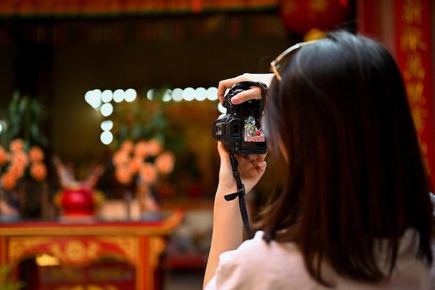 A young Asian female tourist uses her camera to take a photo of a Chinese temple