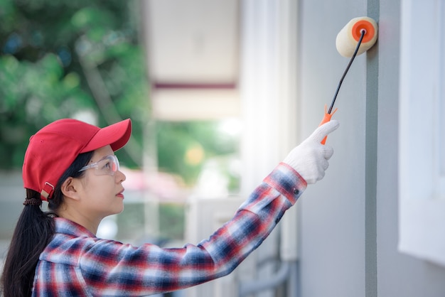 손으로 집의 젊은 아시아 여성 노동자 그림 벽과 회색 또는 시멘트 페인트 페인트 롤러 브러시 페인트
