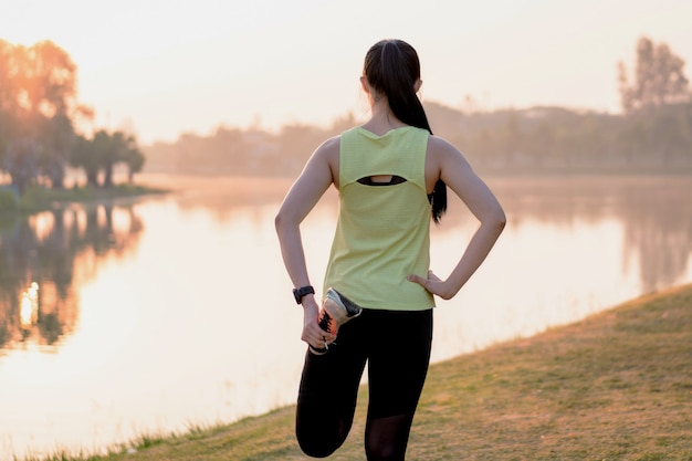 Young Asian female workout before fitness training session at the park under sunlight in the morning. Healthy young woman warming up outdoors. Sport and recreation