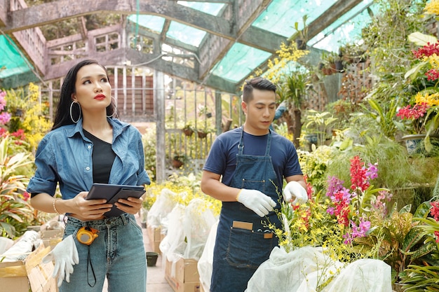 顧客に配達するために植物を集めて梱包する若いアジアの花の苗床労働者