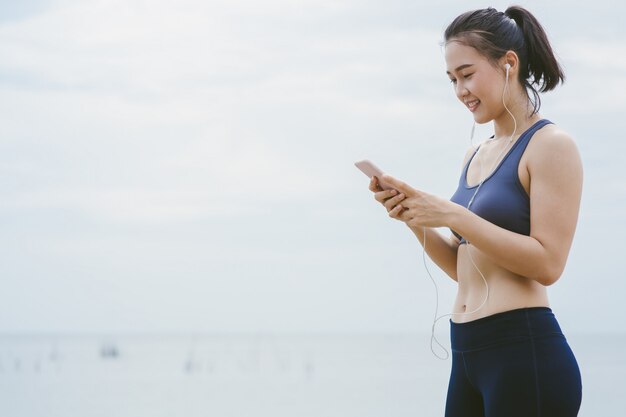 Photo young asian girl choose music for running on the beach.