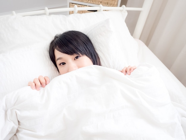 Young asian girl covers her face with white blanket in the morning