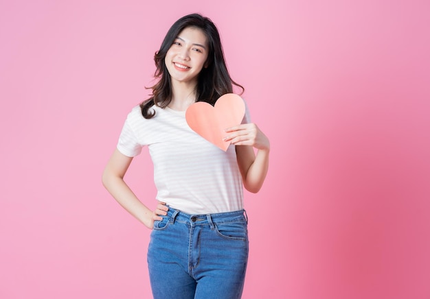 Young Asian girl holding heart shape on pink background