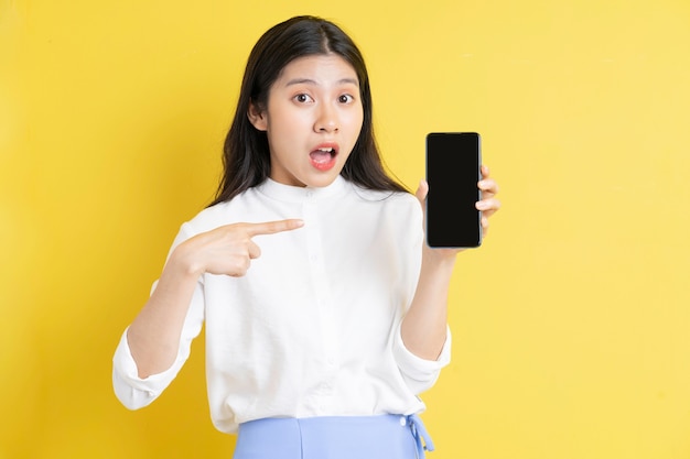 Young asian girl holding phone with expression on yellow background