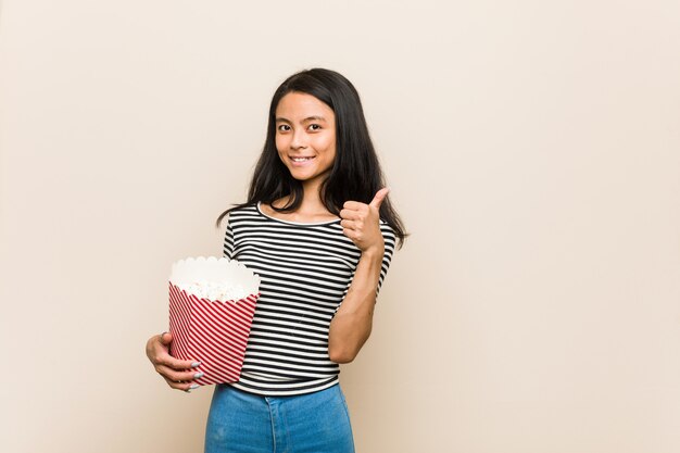 Young asian girl holding a popcorn bucket smiling and raising thumb up