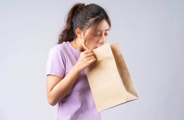 Молодая азиатская девушка давится ртом в бумажном пакете