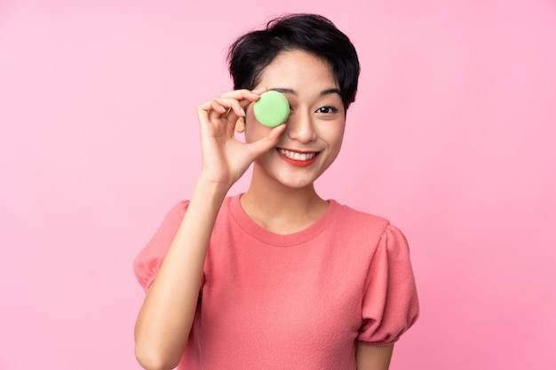 Young Asian girl over isolated pink wall holding colorful French macarons