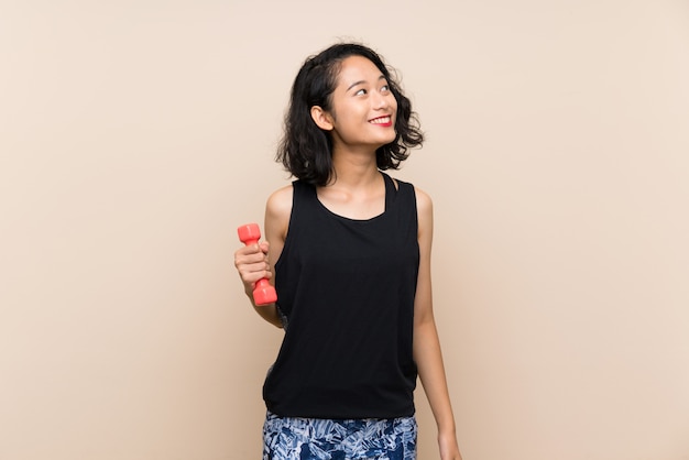 Young Asian girl making weightlifting over isolated wall looking up while smiling