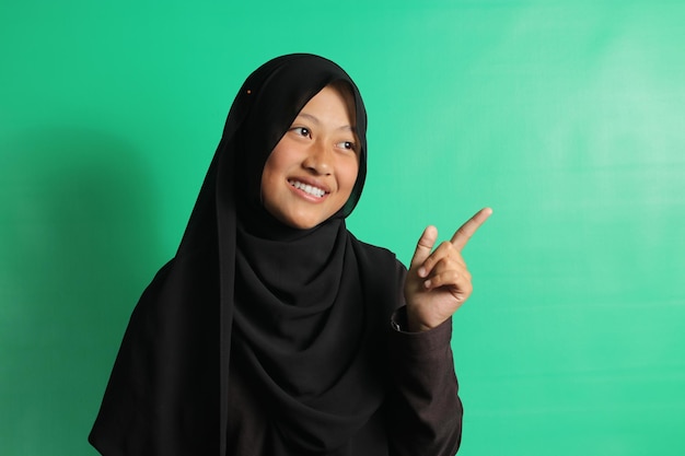 Молодая азиатка показывает пальцем вправо на зеленом фоне