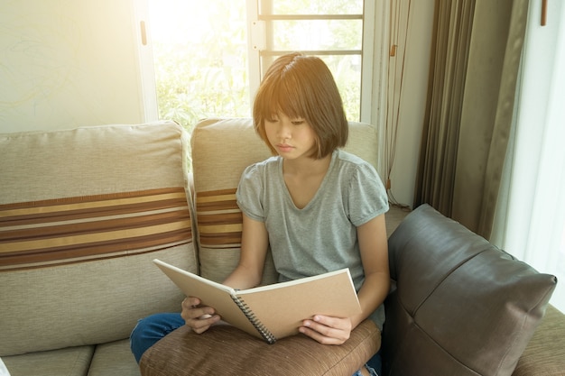 young asian girl read a book on sofa  in living room.