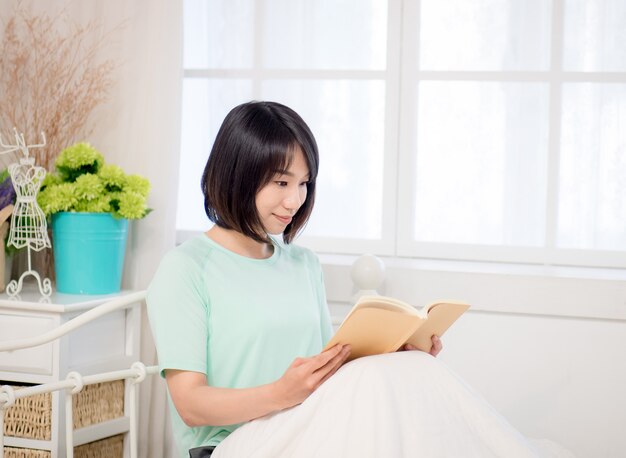 Young asian girl reading a book in bed