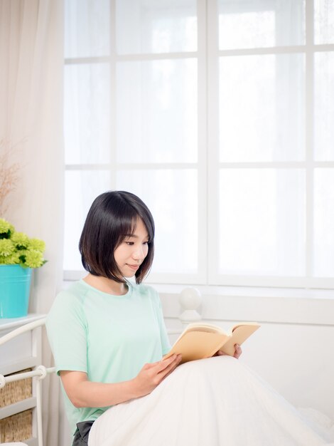 Young asian girl reading a book in bed