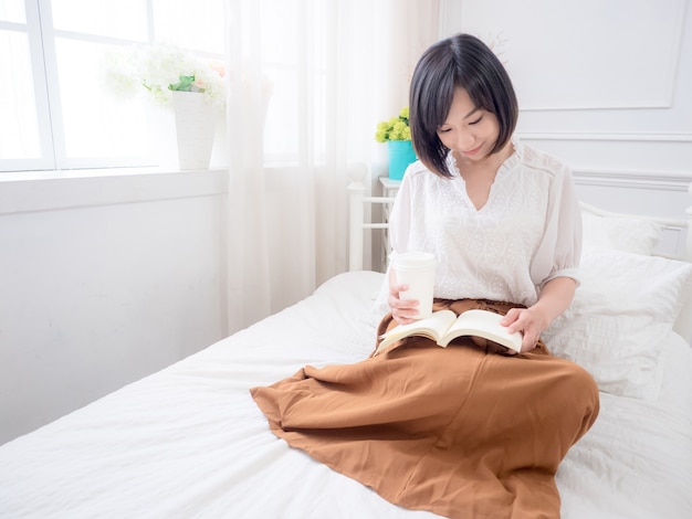 Young asian girl reading a book in bed