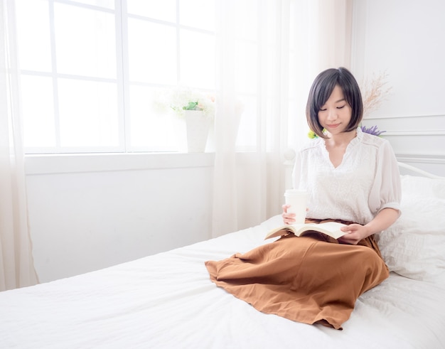 Young asian girl reading a book in bed