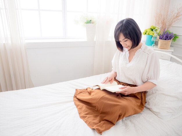 Young asian girl reading a book in bed