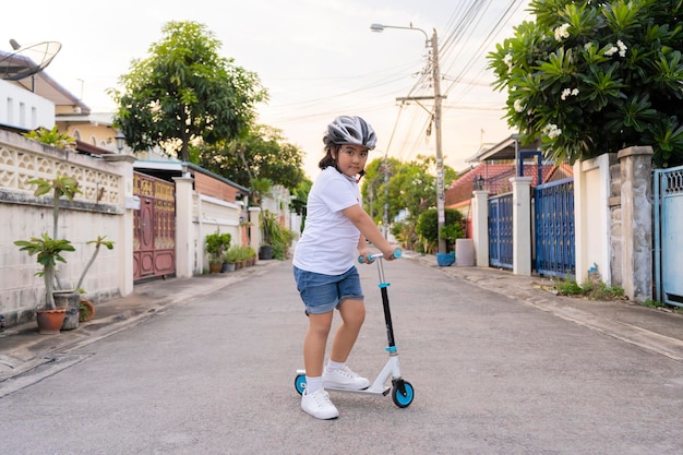 ローラーに乗って安全ヘルメットをかぶった若いアジアの女の子子供たちはスクーターで屋外で遊ぶ子供のためのアクティブなレジャーとアウトドアスポーツ