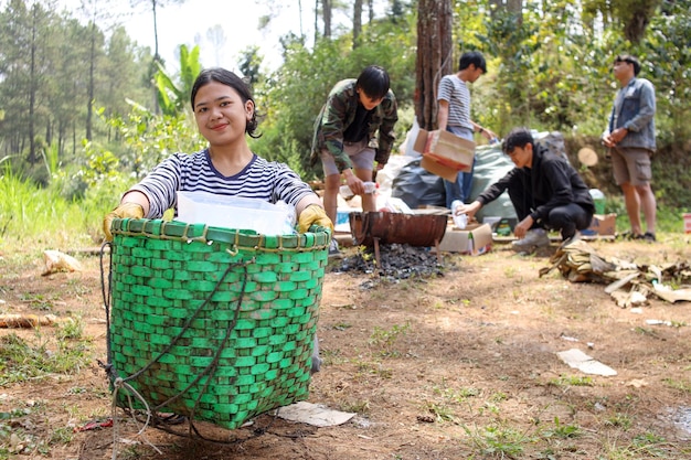 Young Asian girl showing to camera a bag full of trash while friends collecting garbage on the backg