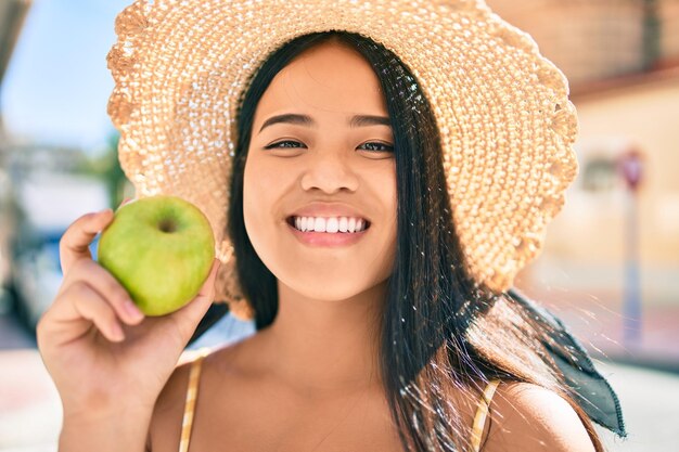健康的な青リンゴを食べて街で幸せな笑みを浮かべている若いアジアの女の子
