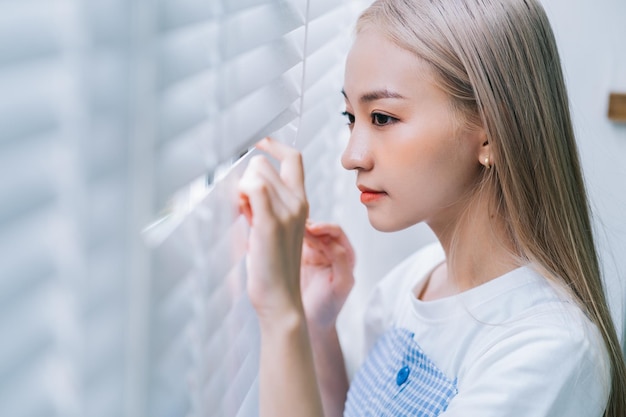 Young Asian girl standing by the window and peeking out