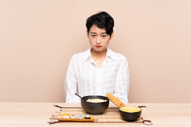 Young Asian girl in a table with bowl of noodles and sushi sad